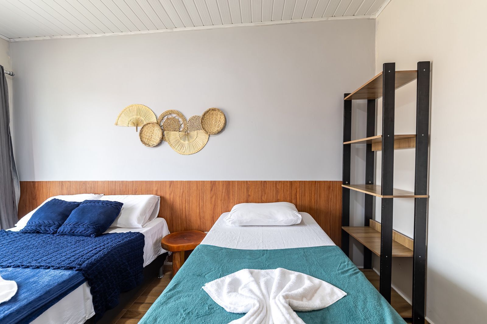 A hotel room with two beds, a wooden headboard, a wall-mounted shelf, and a small wooden stool.
