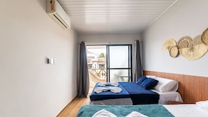 Habitación de hotel con una cama, una segunda cama, una ventana con cortinas, una hamaca afuera y un adorno en la pared.