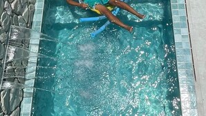 Un hombre en una piscina con tobogán acuático, rodeado de muros de piedra y suelo de baldosas.