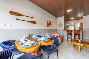 A dining area with round wooden tables, blue upholstered chairs, and a sofa. There are two wooden paddles on the wall and a framed picture above the sofa.