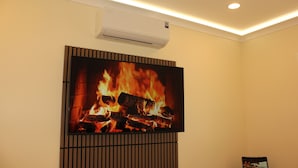 Habitación con una televisión de pantalla plana montada en la pared, un equipo de aire acondicionado encima y un panel de madera debajo.