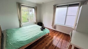 Una habitación con cama, una mesita y dos ventanas.