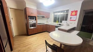 Una cocina moderna con armarios de madera, horno empotrado, microondas y cocina a gas. Hay una mesa de comedor blanca con una silla.