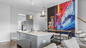 A modern kitchen with a central island, a dining area with bar stools, and a large neon sign on the wall. - Gulch Large Group Home! Rooftop! Walkable! Views! (Nashville)