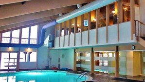 An indoor swimming pool with a glass ceiling, a lounge area, and a staircase leading to an upper level. - Chalet Retreat Hot Tub, Theater, Arcade & Firepits (Big Bass Lake)