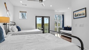 A hotel room with two beds, a ceiling fan, a cityscape painting, and a view of the outdoors.