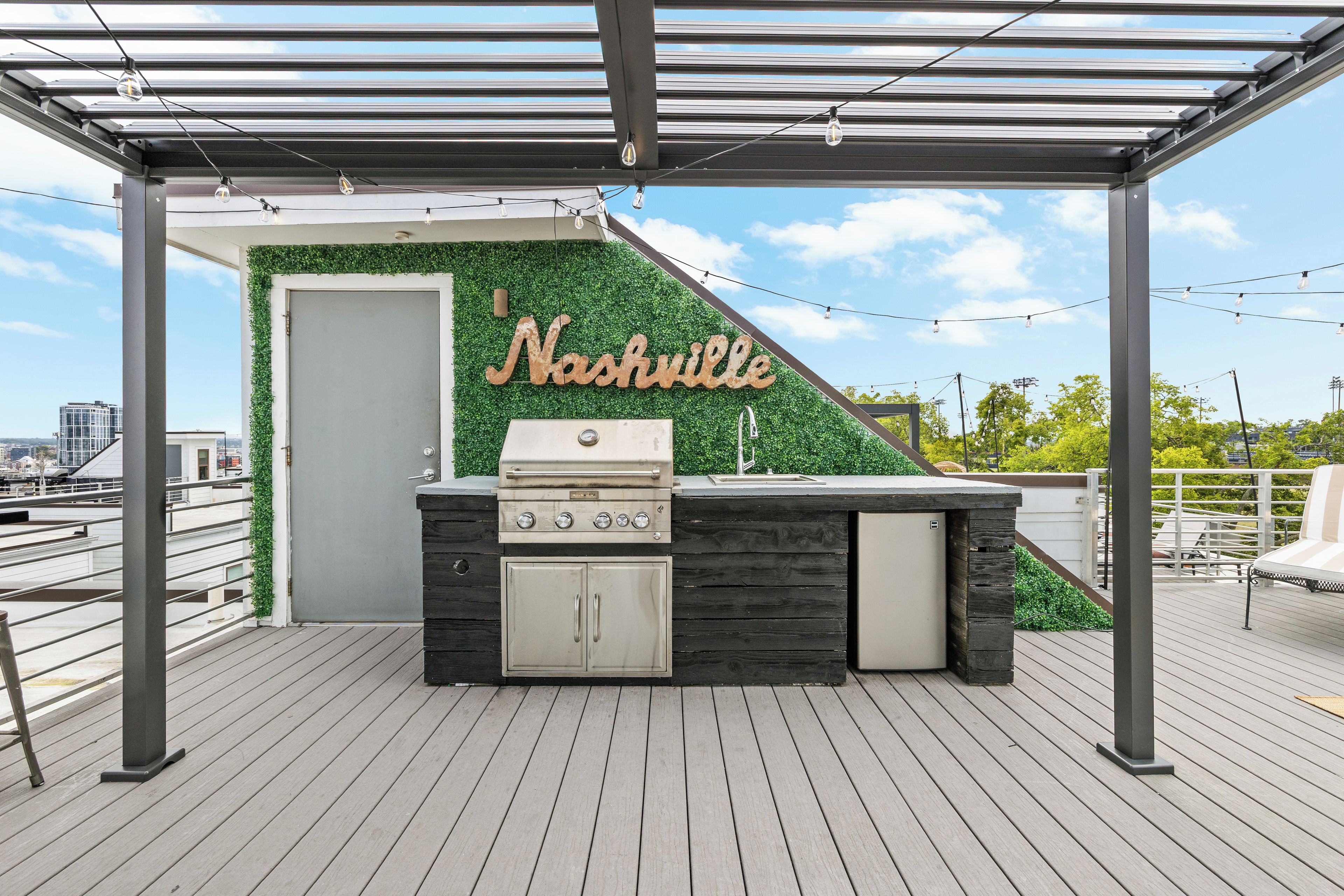 Een buitenbarbecueplaats met een grill en een spoelbak, omgeven door een pergola en een muur begroeid met planten.