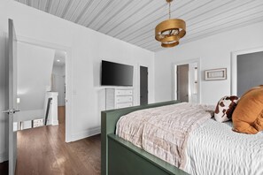 A bedroom with a bed, a television, a dresser, and a door leading to another room.