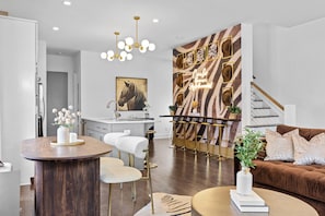 A modern living room with a brown sofa, a round coffee table, and a dining area with a wooden table and white chairs. - Walk to Broadway / Rooftop w/ City Views / 14 beds (Nashville)
