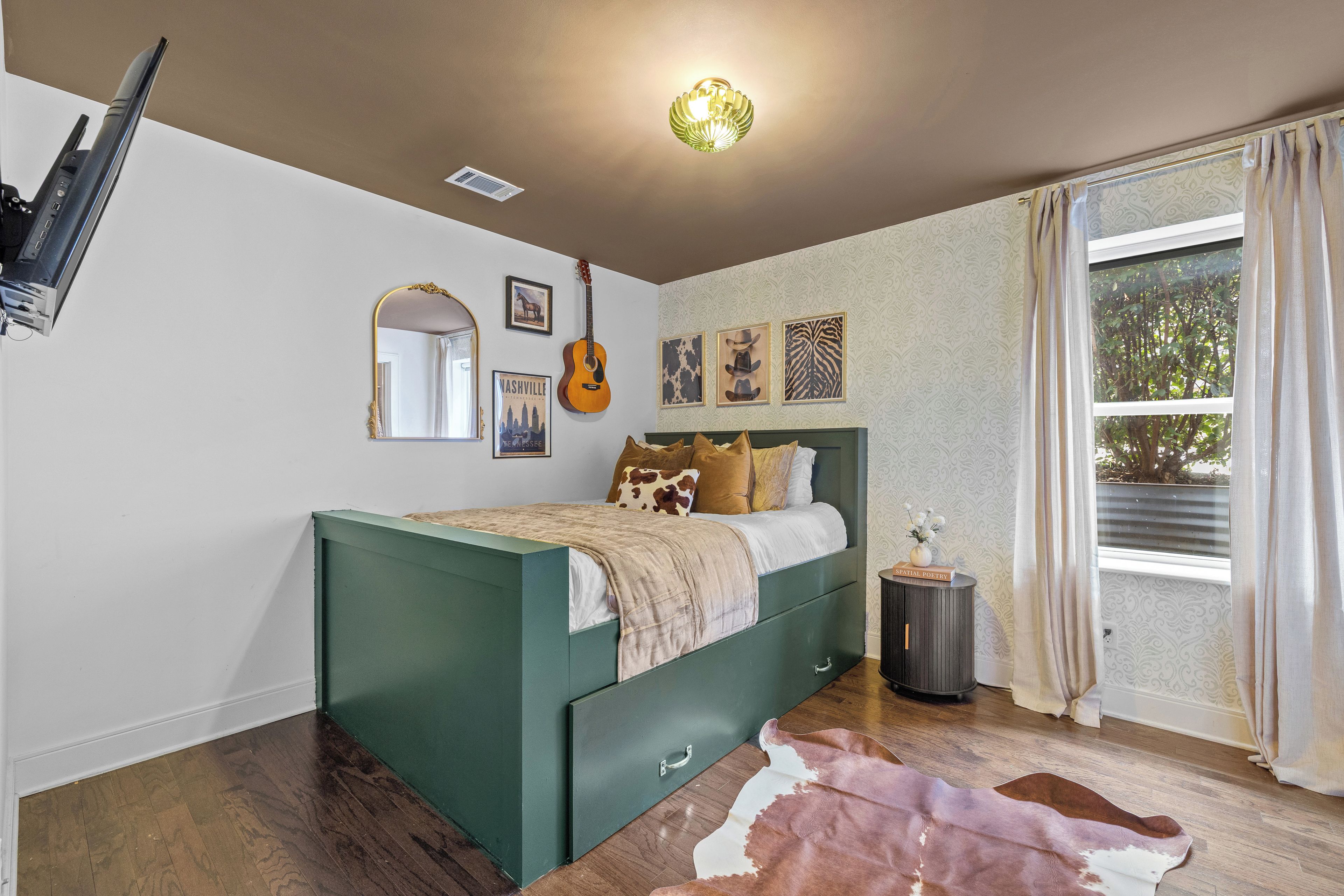 A bedroom with a green bed, a guitar, a mirror, and wall art.