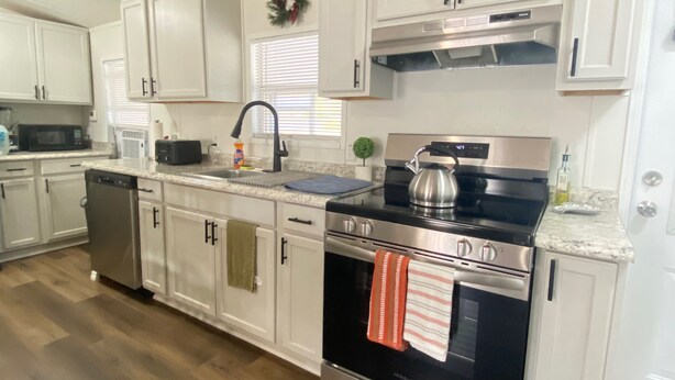A modern kitchen with white cabinets, stainless steel appliances, and a wooden floor.