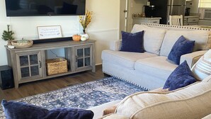 A living room with a large flat-screen TV, a sofa set, a wooden console table, and a patterned rug.