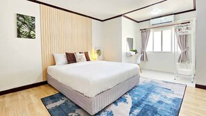 A bedroom with a large bed, a window with curtains, a wall-mounted air conditioner, and a small side table with a plant. - Greta Villa  Nakluea 18 (Pattaya)