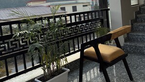 A balcony with a potted plant, a chair, and a view of a building and hills in the background. - Casa garden Aamwala (Dehradun)