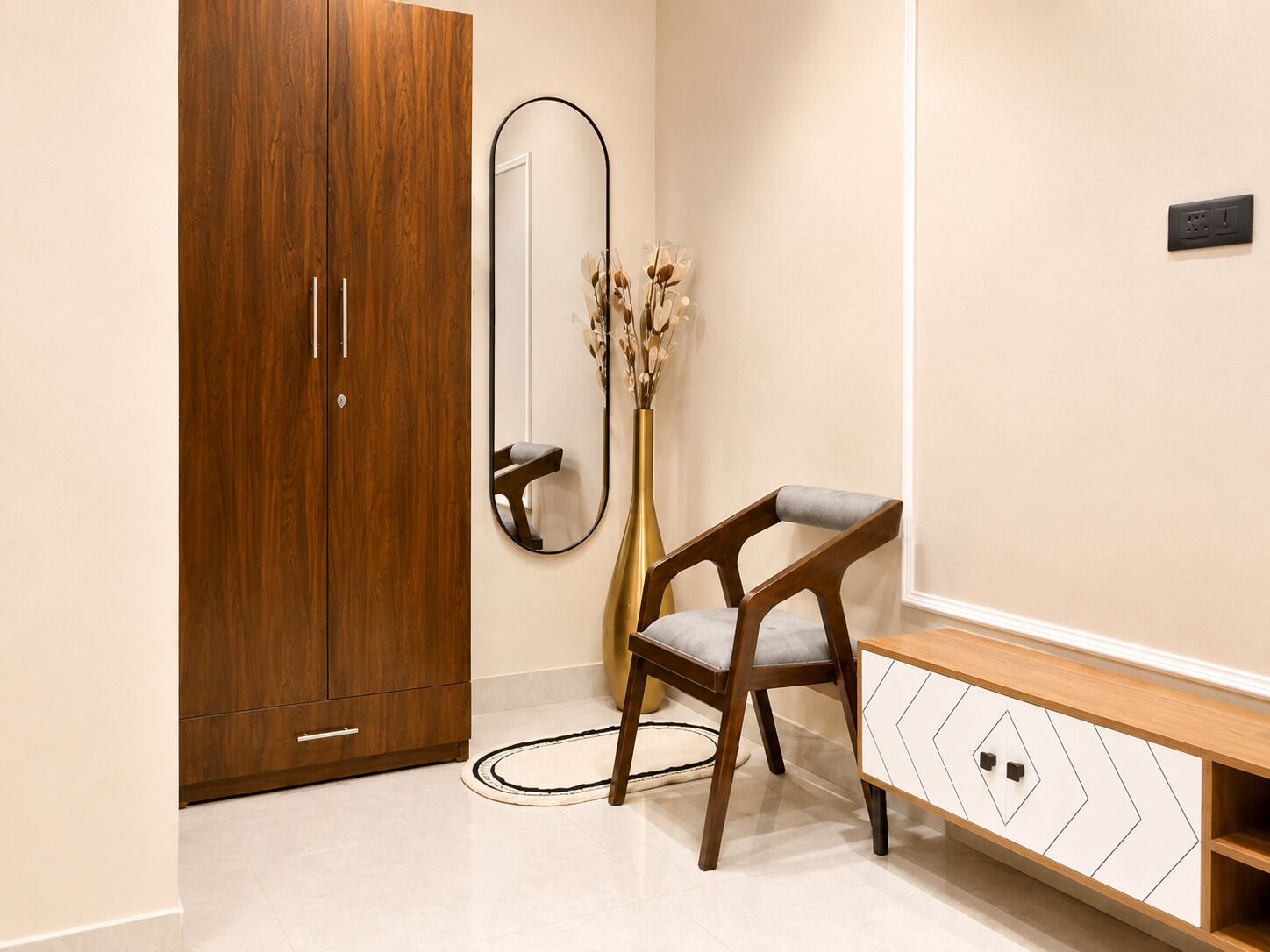 A room with a wooden wardrobe, a mirror, a vase with dried flowers, a chair, and a wooden console table.