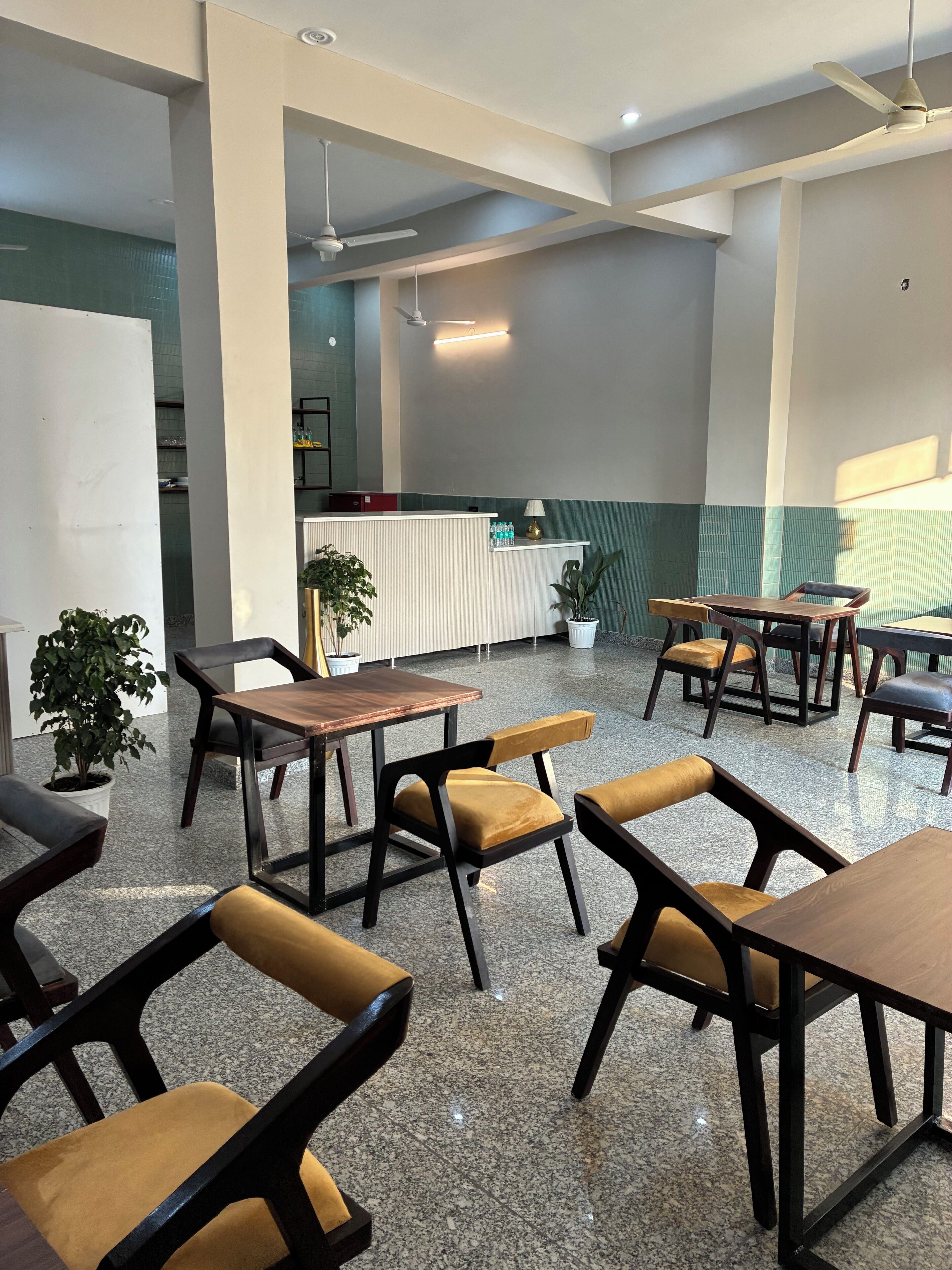 Un espace intérieur spacieux, doté de plusieurs tables et chaises, d’un comptoir d’accueil et de plantes en pot.