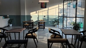 A modern indoor space with tables and chairs arranged for dining, large windows allowing natural light, and a ceiling fan. - Casa garden Aamwala (Dehradun)
