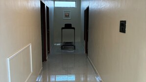 A hallway with a tiled floor, a ceiling light, a framed picture on the wall, and a door at the end. - Casa garden Aamwala (Dehradun)