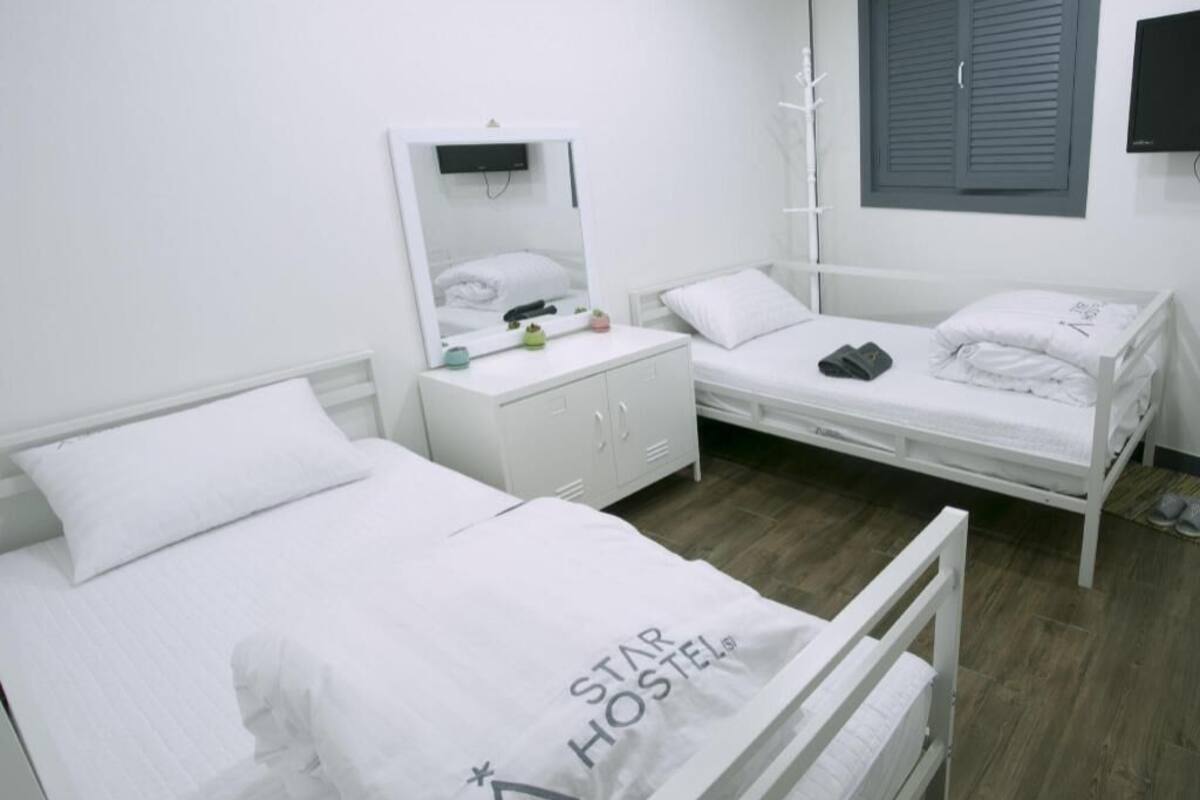 A room with two beds, a white dresser, a mirror, a coat rack, and a television.