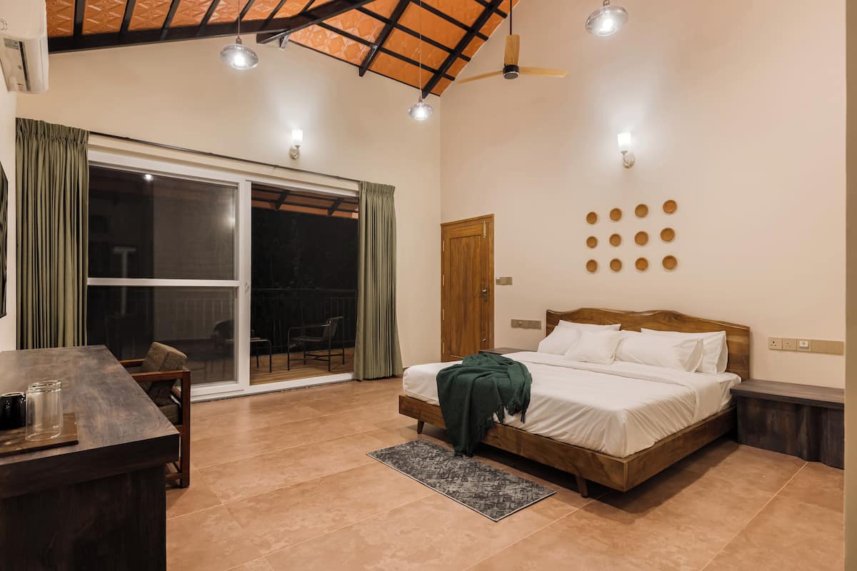 Un dormitorio con cama, escritorio, silla, ventilador de techo y un amplio ventanal con cortinas.