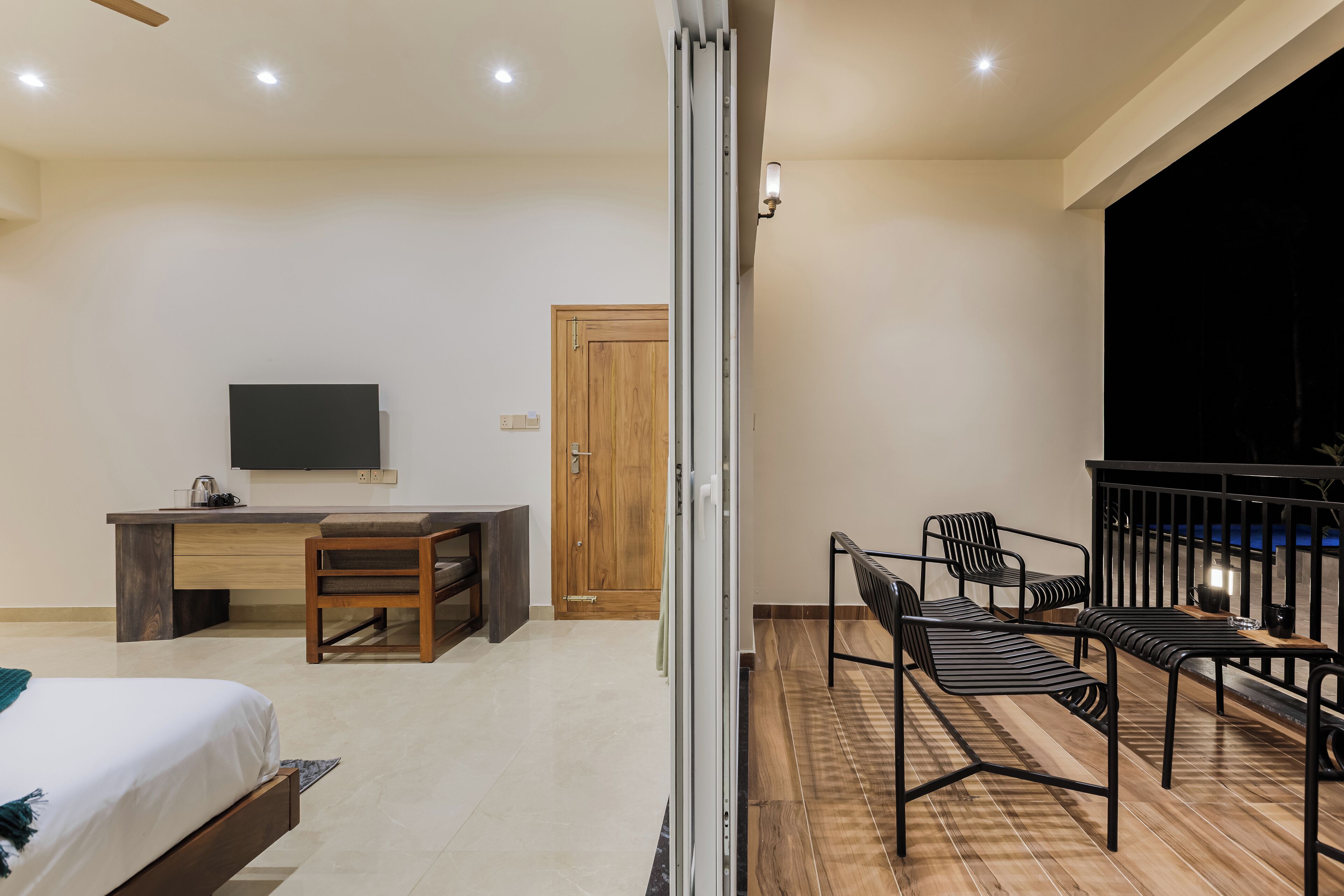 Un dormitorio moderno con cama, escritorio y televisor. Cuenta con un balcón con sillas y una mesa.