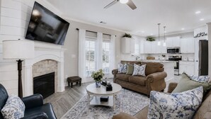 Ein Wohnzimmer mit Kamin, Fernseher, Deckenventilator und einer Küche im Hintergrund.