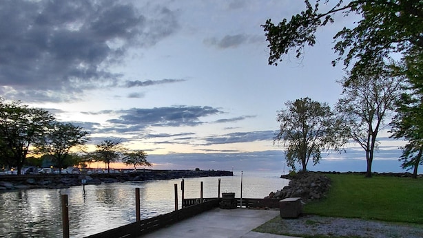 Une terrasse extérieure avec un foyer, deux chaises et une vue sur une étendue d’eau.
