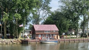 Une maison en bois avec un toit rouge, située au bord d’un lac paisible, avec un bateau amarré et des canards qui nagent.