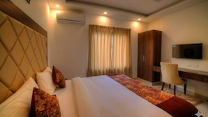 A hotel room with a large bed, a desk, a chair, a television, and a ceiling fan. - Hotel Peridot Near Delhi Airport (New Delhi)
