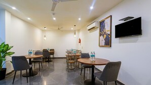A conference room with round tables, chairs, a ceiling fan, recessed lighting, an air conditioning unit, a flat-screen TV, and a framed artwork on the wall. - Hotel Peridot Near Delhi Airport (New Delhi)