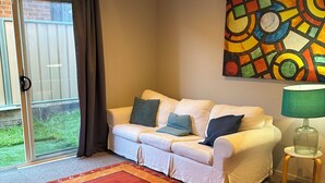 A living room with a white sofa, a red rug, a green lamp, and a colorful abstract painting on the wall. - Pearly shells central Nelson Bay. (Nelson Bay)