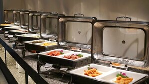 Montaje de bufé con diversos alimentos en bandejas, incluyendo mariscos, ensaladas y frituras.