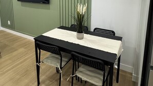 Een eetgedeelte met een tafel en stoelen, een flatscreen televisie aan de muur en een decoratieve plant in een vaas.