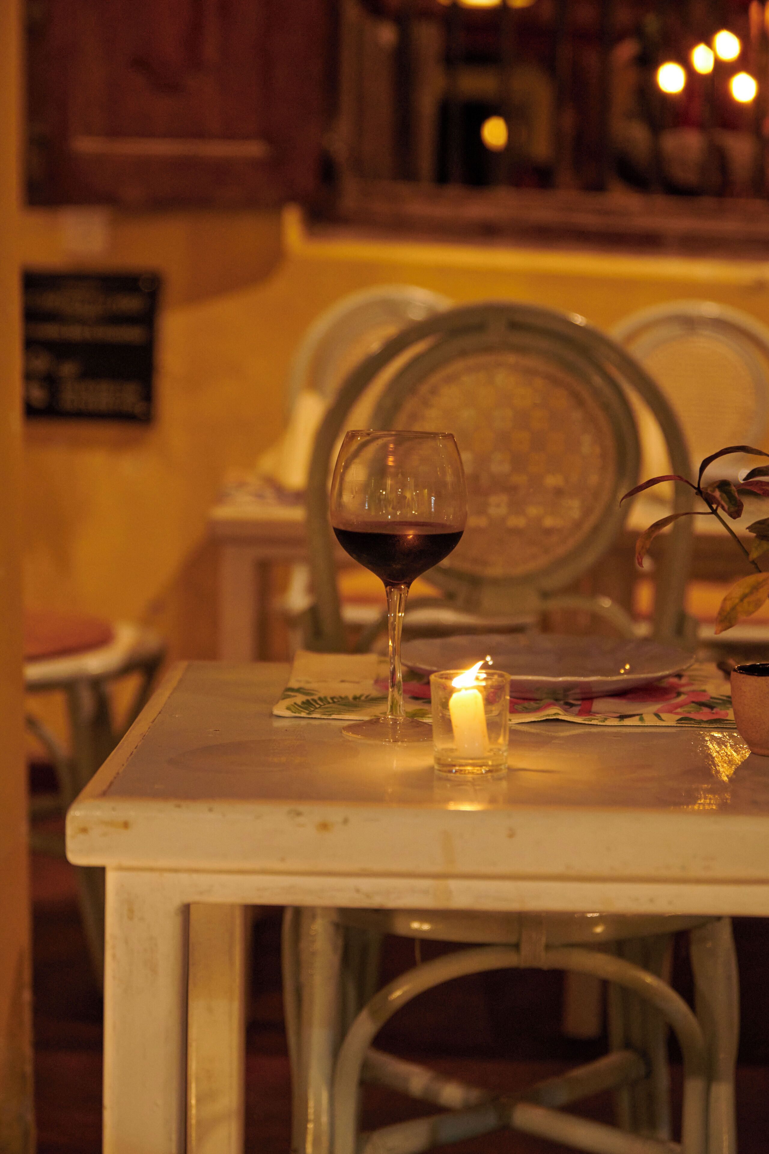 A table with a glass of red wine, a lit candle, and a menu.