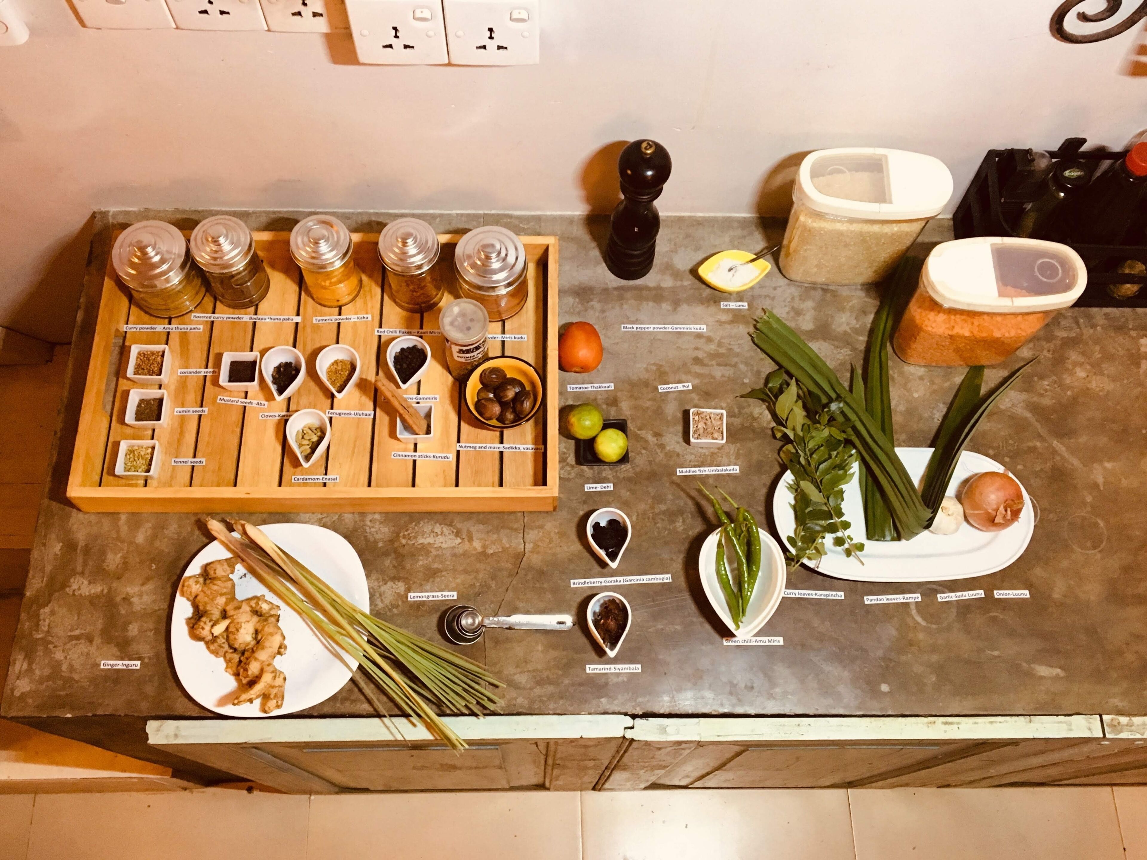 A kitchen counter with various spices, a pepper grinder, a cutting board, and a plate of ginger.