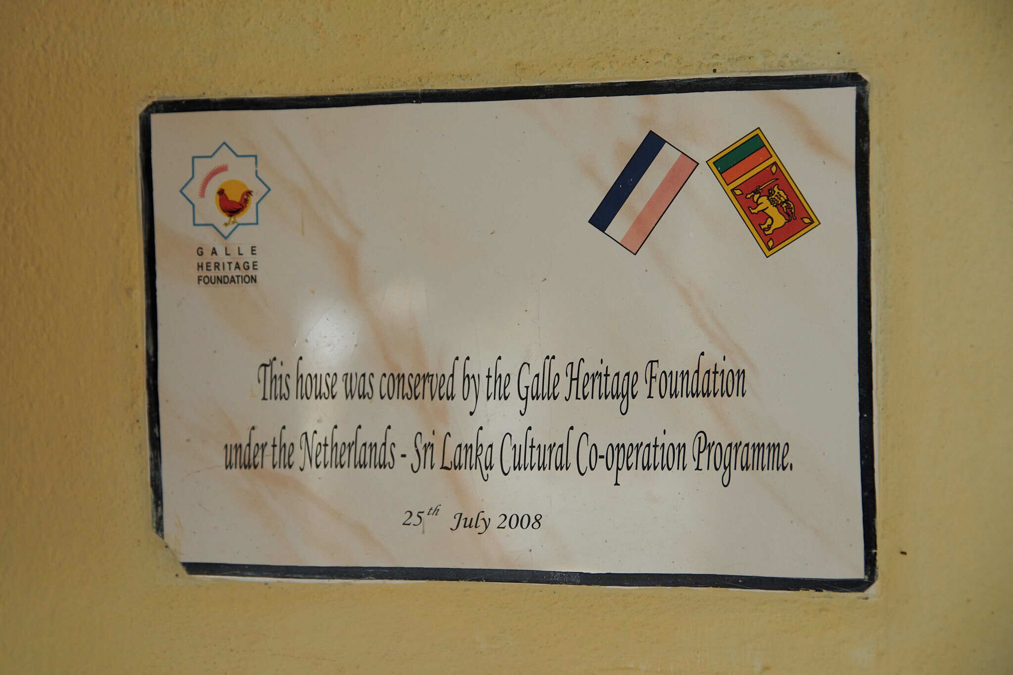Eine Tafel an der Wand mit Text über die Galle Heritage Foundation und Flaggen.