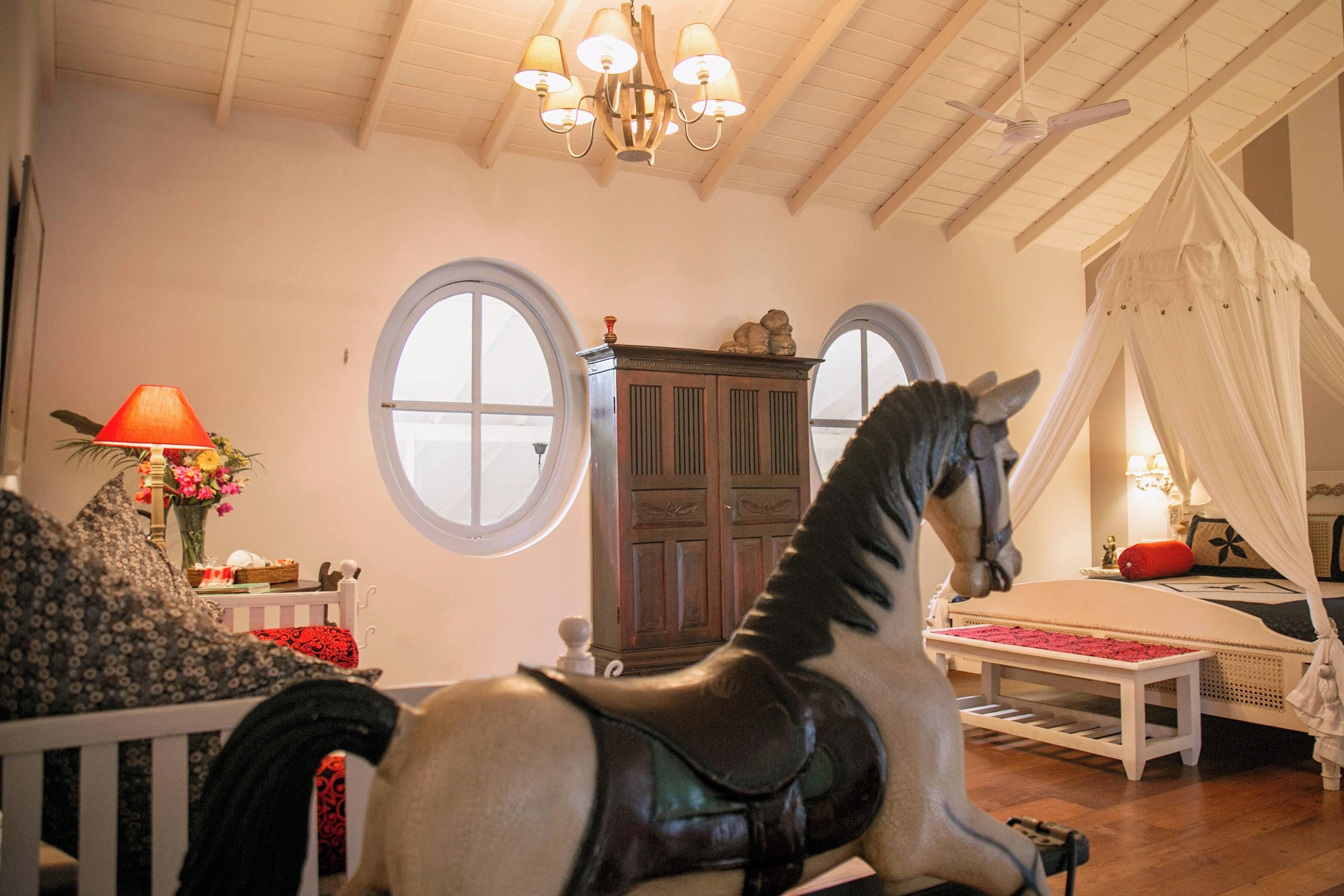 A room with a wooden ceiling, a chandelier, a bed with a canopy, a rocking horse, and a cabinet.