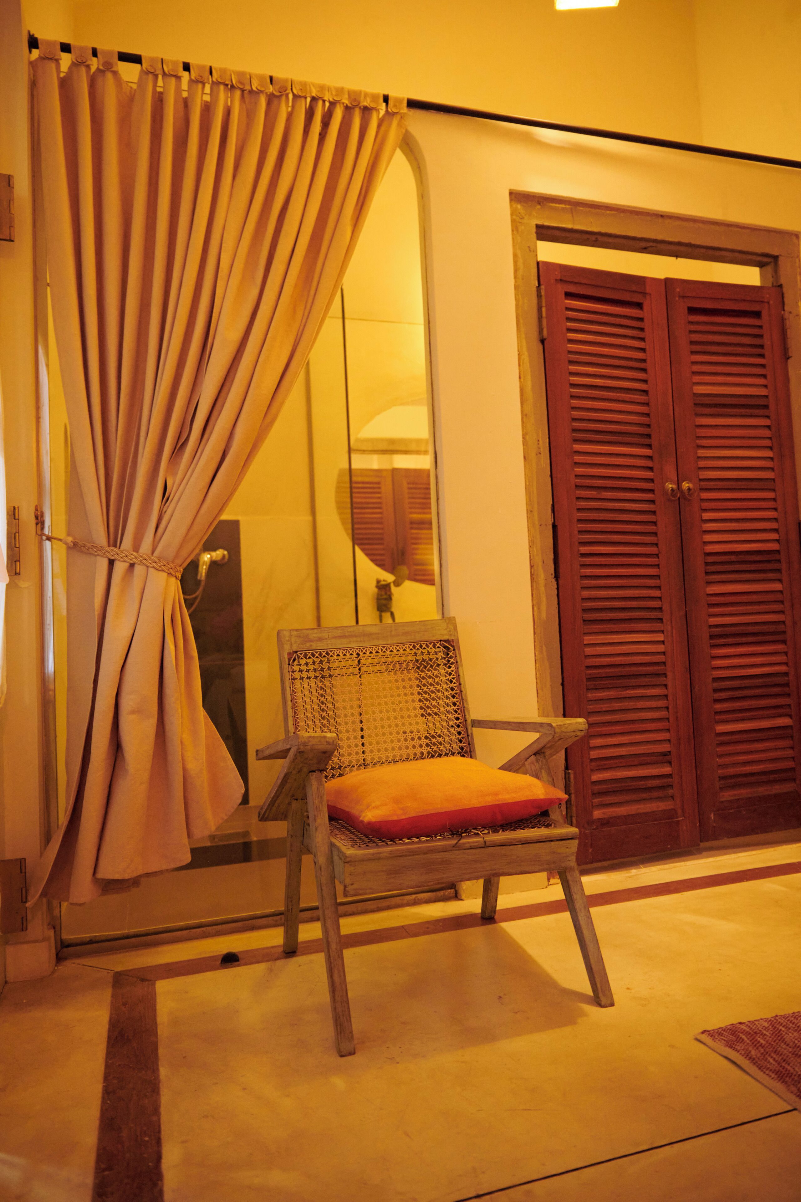 A room with a wooden chair, a wooden door, and a curtain.