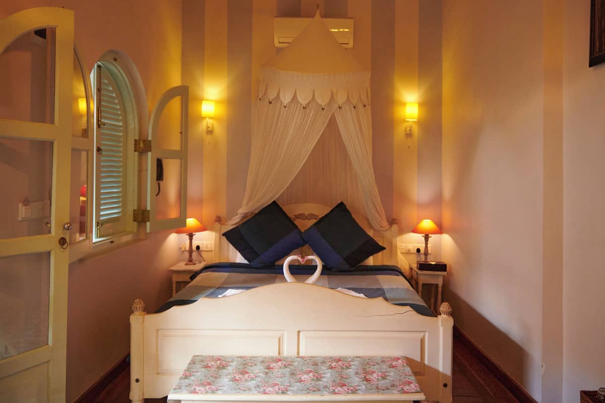 Une chambre à coucher avec un lit à baldaquin, des lampes de chevet, une couvre-lit à motifs floraux et un miroir avec une porte.