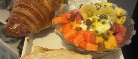 Una bandeja con un croissant, una ensalada de frutas, un huevo duro y dos tostadas.