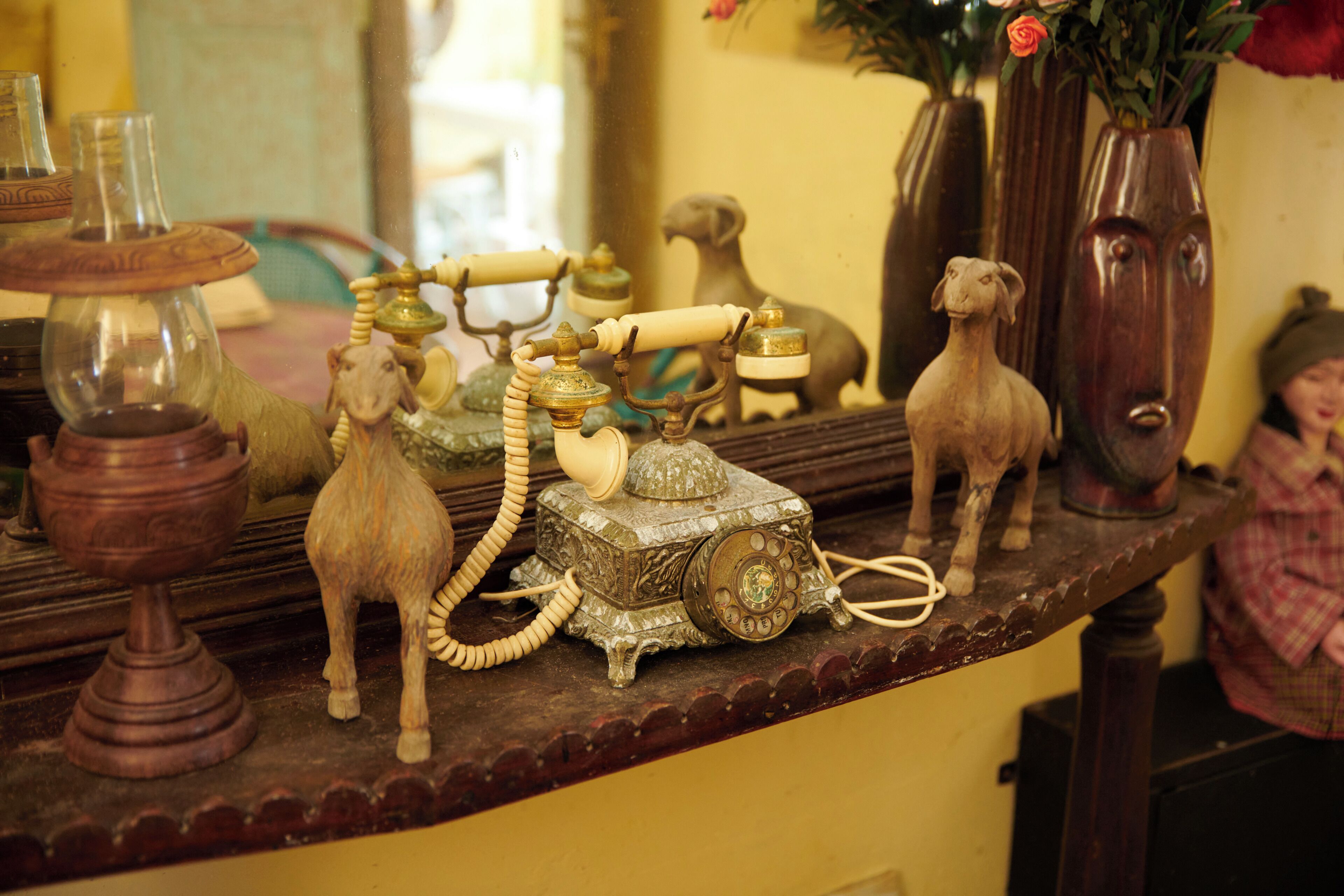 A shelf with various antique items including a rotary phone, a goat figurine, and a vase with flowers.