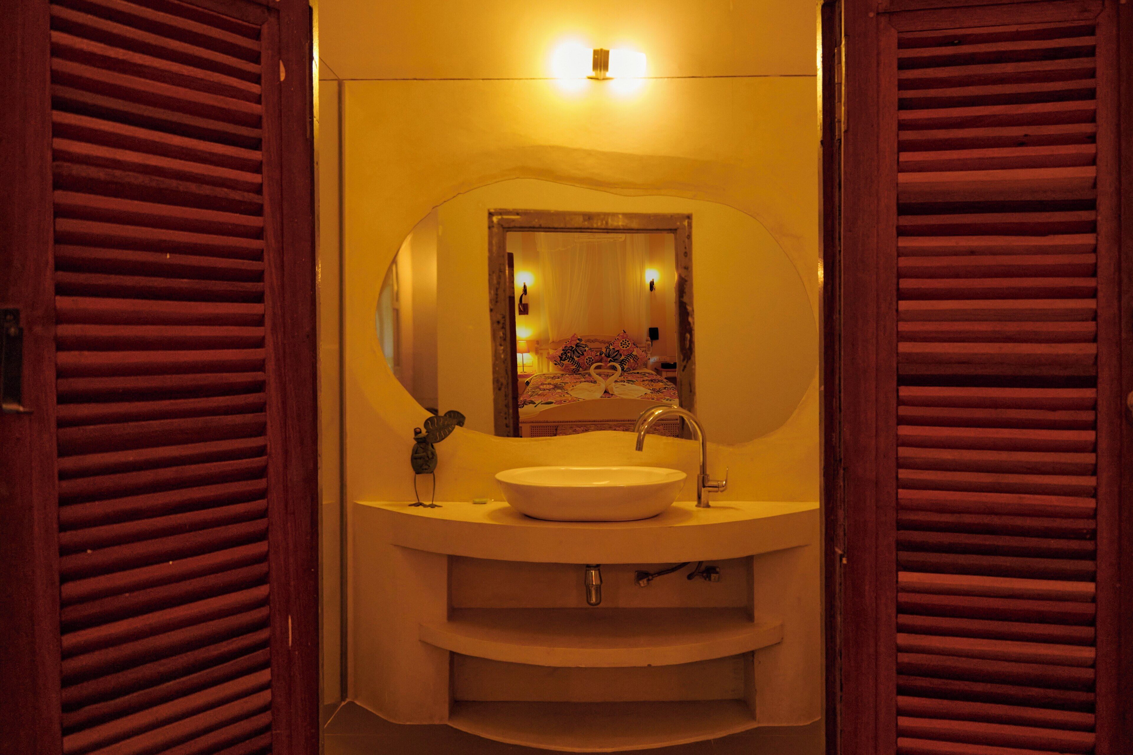 A bathroom with a round sink, a mirror, and wooden shutters.
