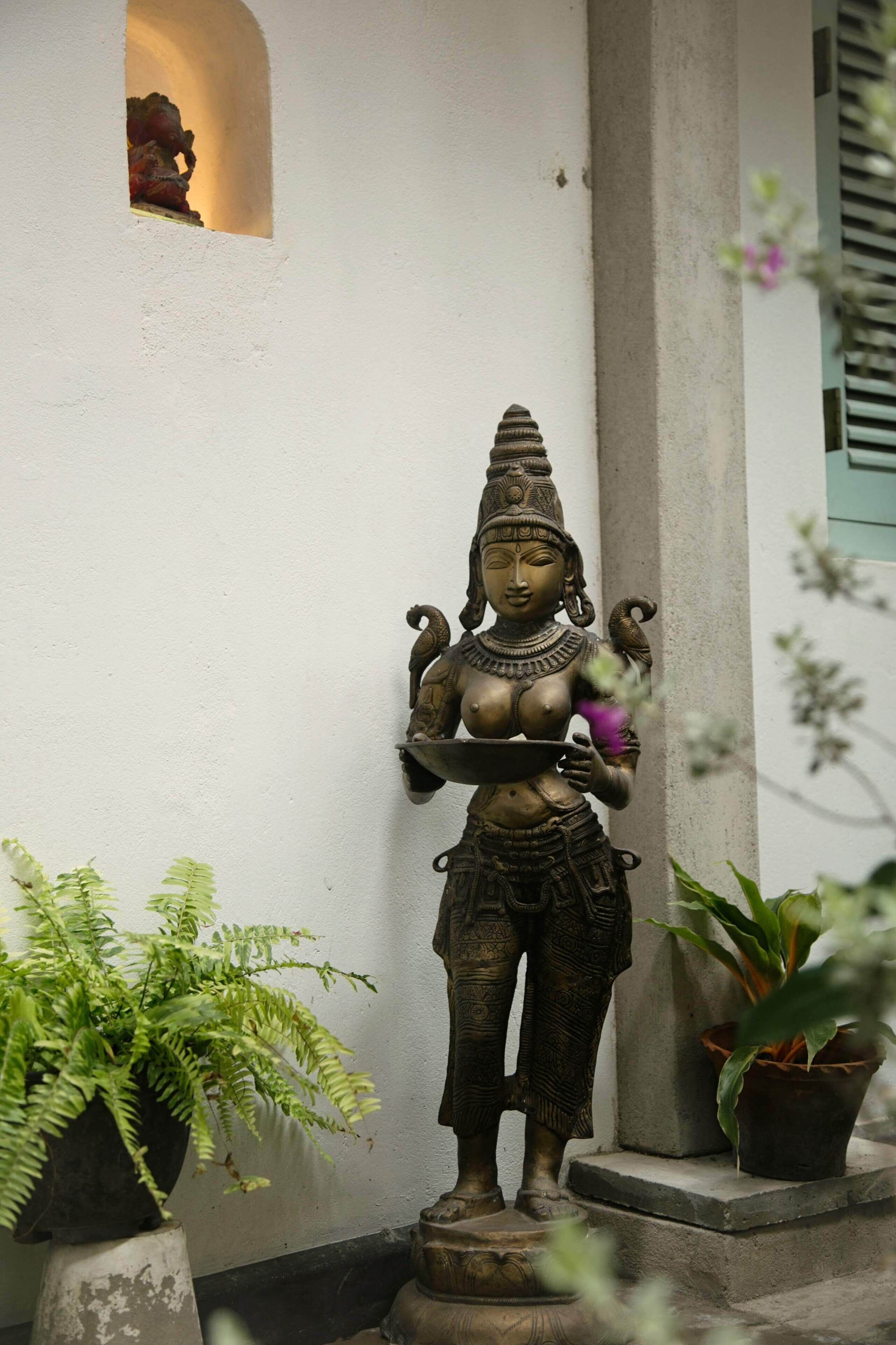 A statue of a deity in a courtyard with potted plants and a column.