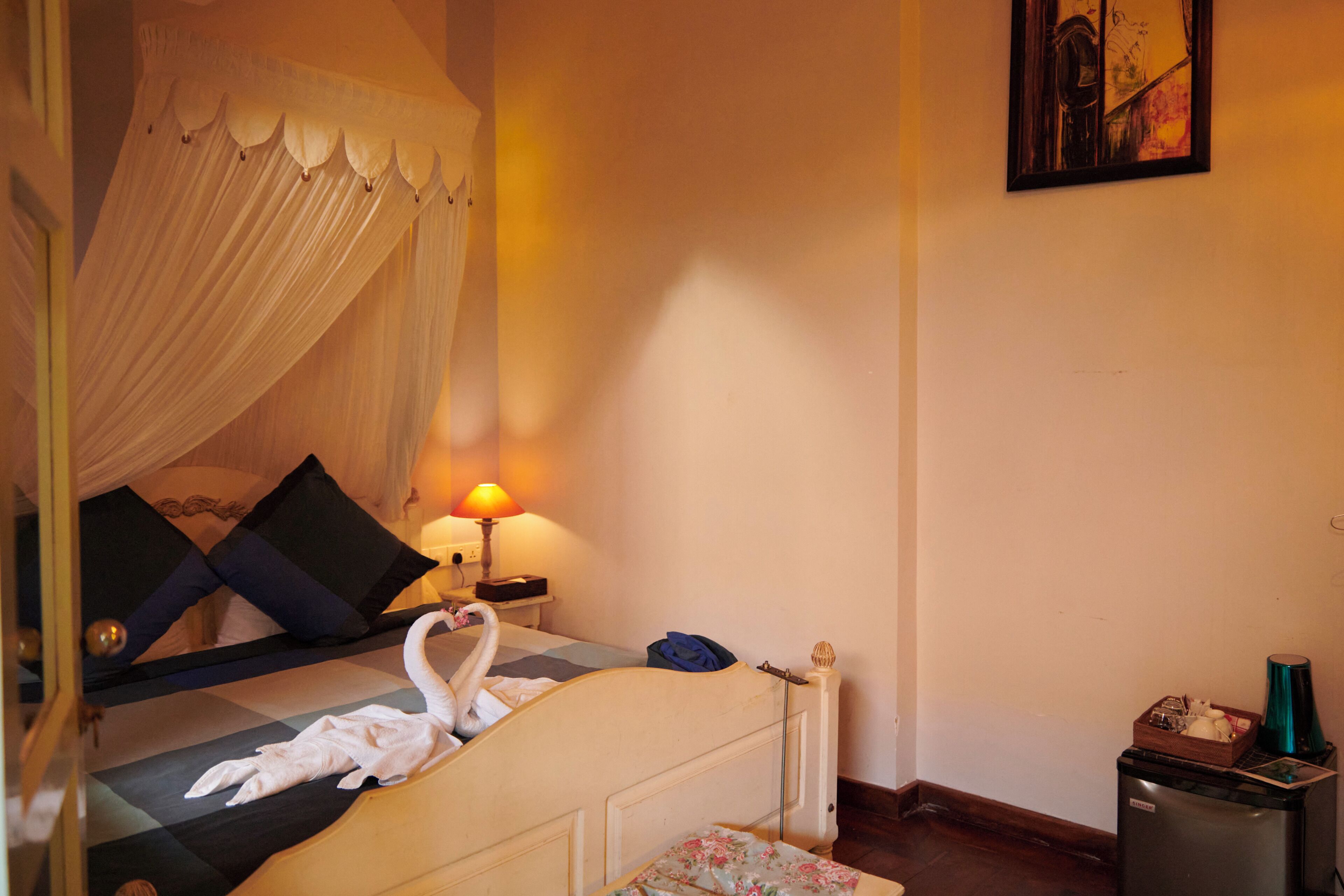 A bedroom with a canopy bed, a bedside table with a lamp, and a small cabinet.