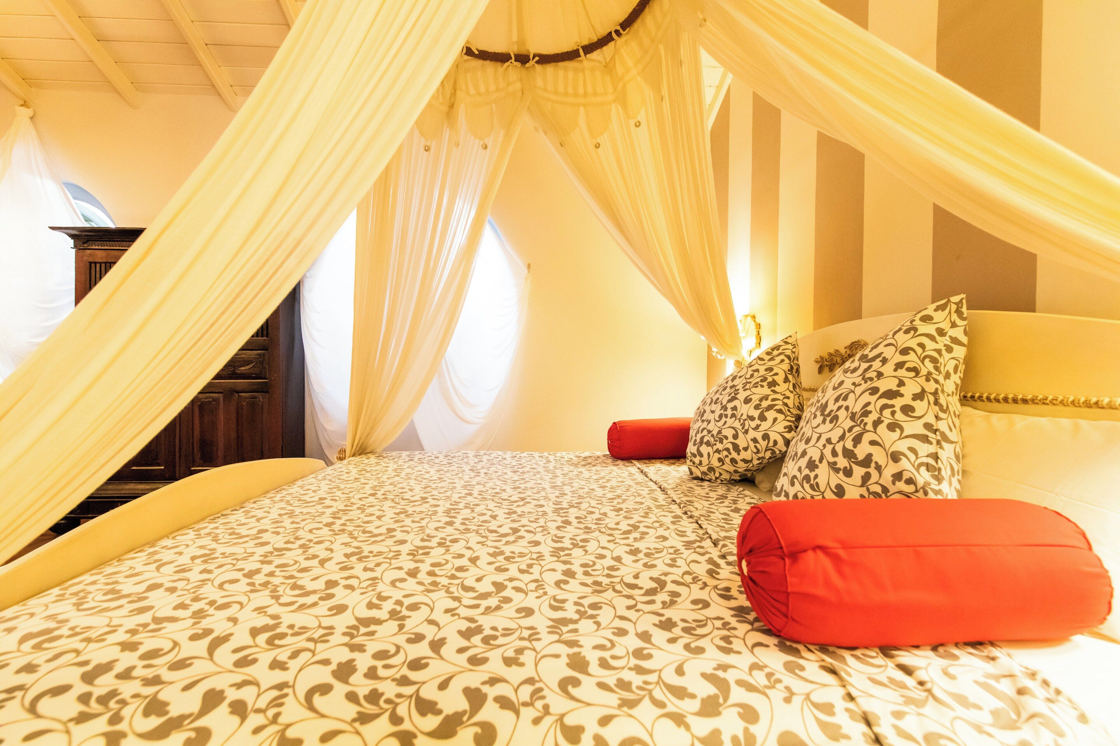 Un dormitorio con cama a dosel, ropa de cama estampada y una mesita de noche con lámpara.