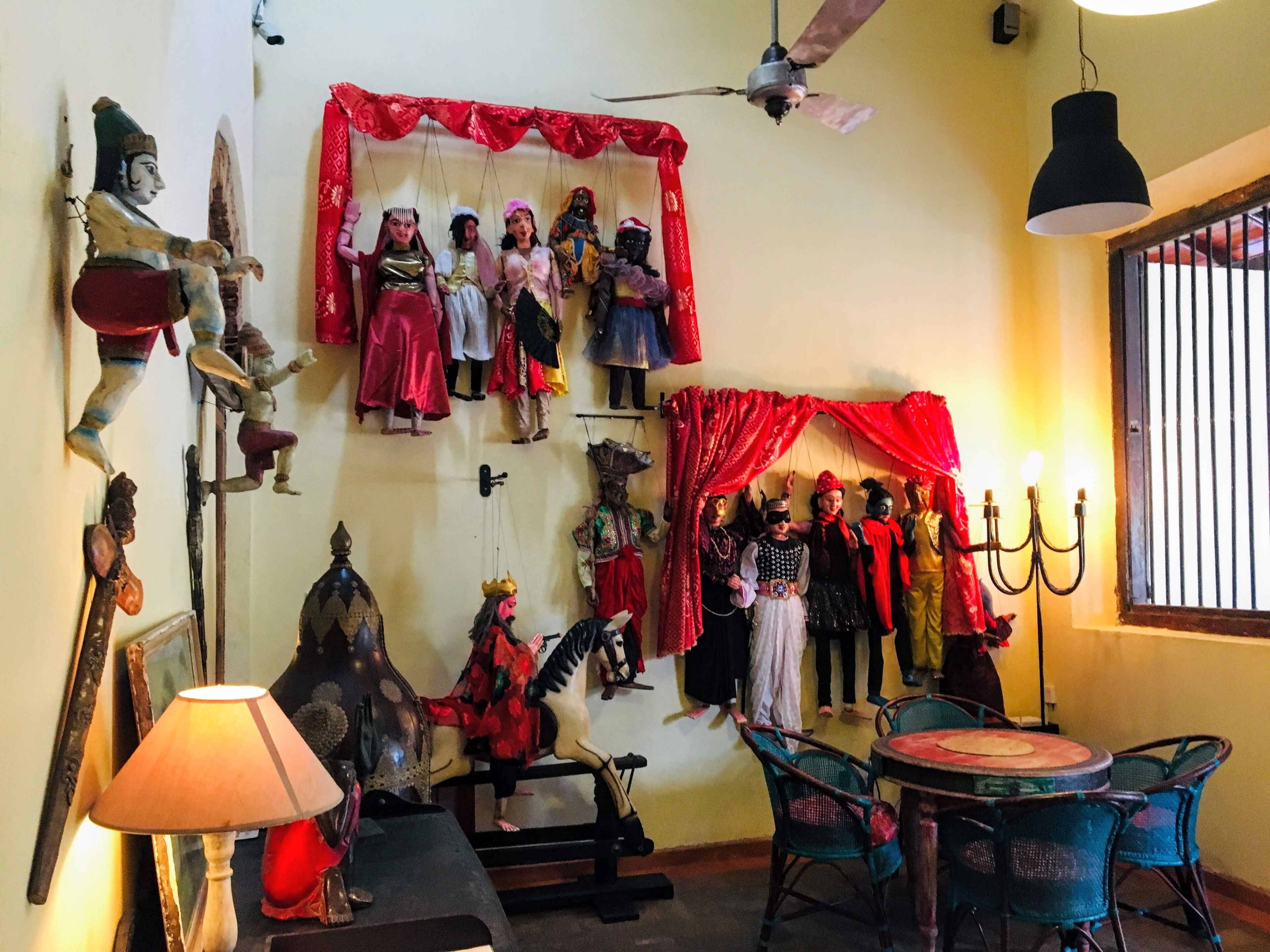 A room with a ceiling fan, a table with chairs, a lamp, and a wall decorated with various figures and a horse.