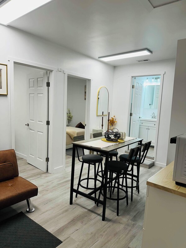 A modern, well-lit room with a dining area featuring a table and chairs, a sofa, and a kitchen area with a refrigerator. - Renton’s most peaceful neighborhood - Comfort & Quiet (Renton)
