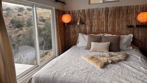 A bedroom with a large window, a wooden wall panel, and a bed with patterned bedding and pillows. - Lake Haus 59 : Family-friendly 2bed/2ba, Full Kitchen + Lake View Deck (Friant)