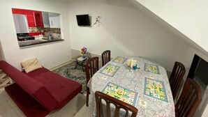 Un ambiente compatto con angolo ristoro, angolo cottura e divano rosso.