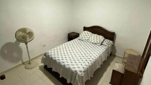 Una camera da letto con un letto, un comodino, una ventola a piantana e un armadio.